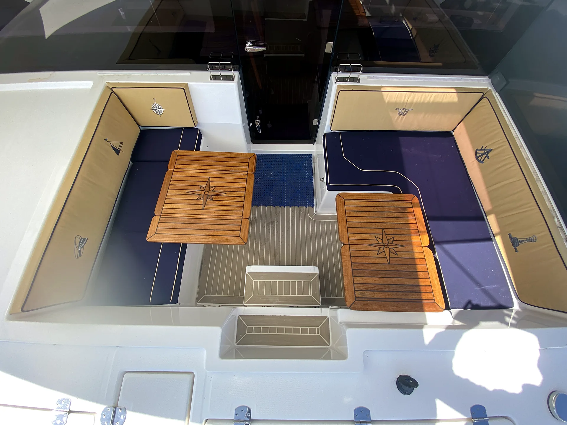 Forward cockpit lounge with navy and sand cushions and teak compass-rose tables